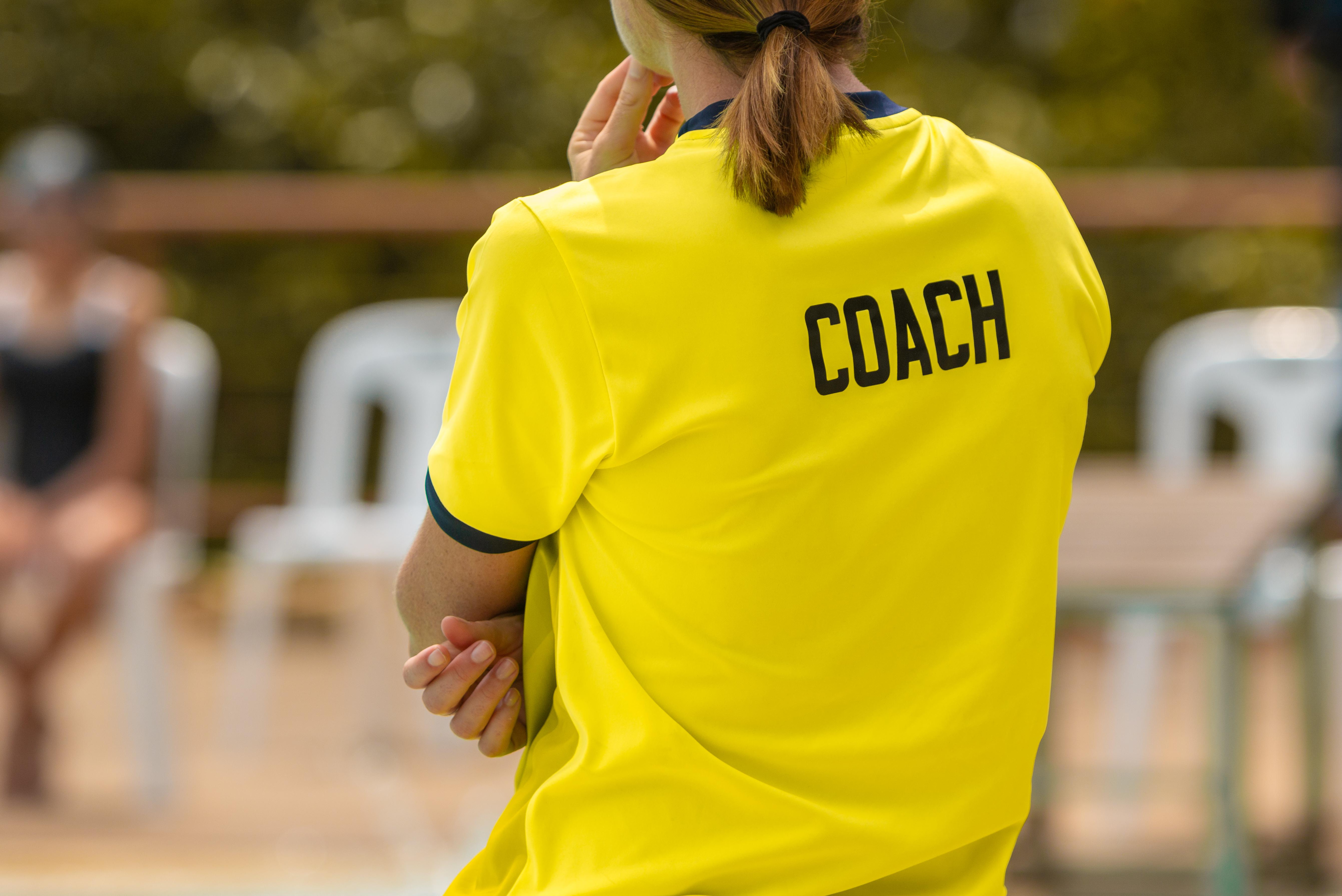 Coach in yellow jersey stands on sideline, background blurred
