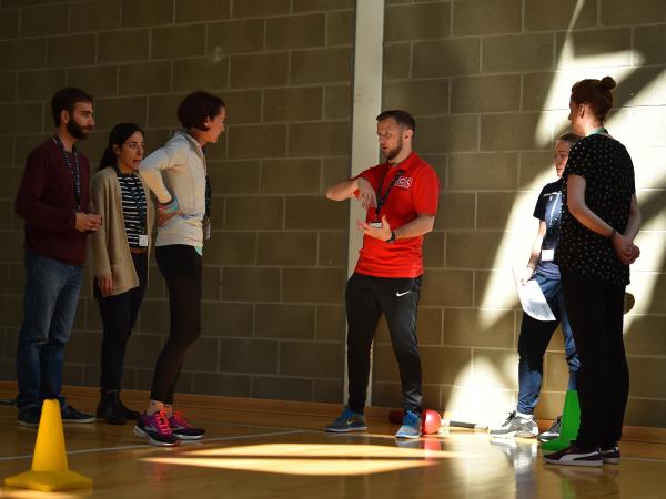 A coach addresses a group of students in a sports hall