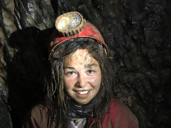 Girl smiling at camera wearing caving equipment underground