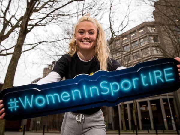A woman holding a #WomenInSportIRE sign