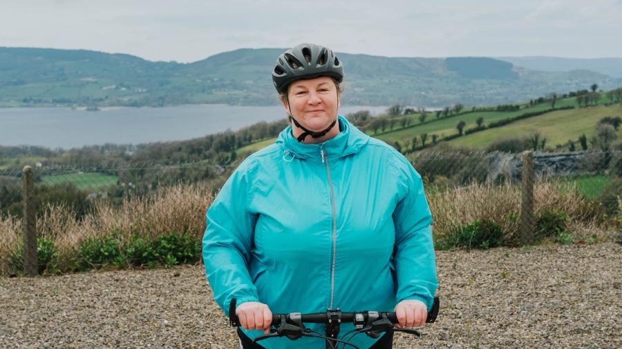 Noreen sits on her bicycle looking at the camera with mountains in the background