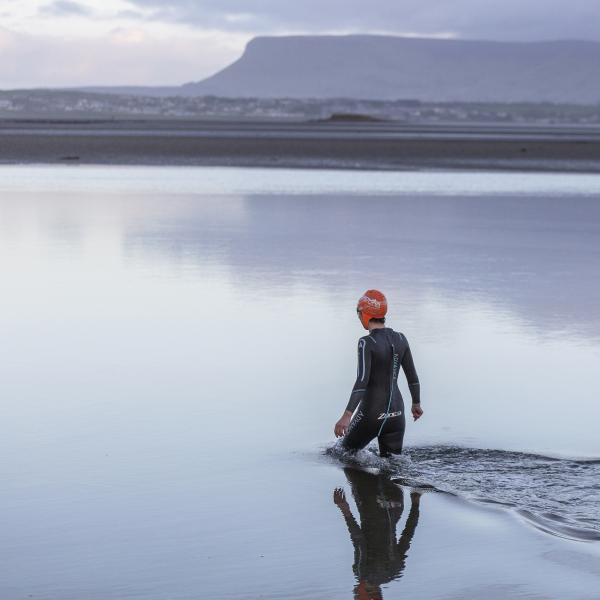 Swimmer walks in to the sea with the mountains in the background