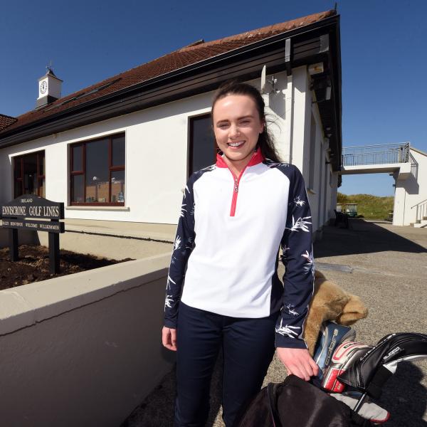 Sophie stands outside the club house with her hand on her golf bag