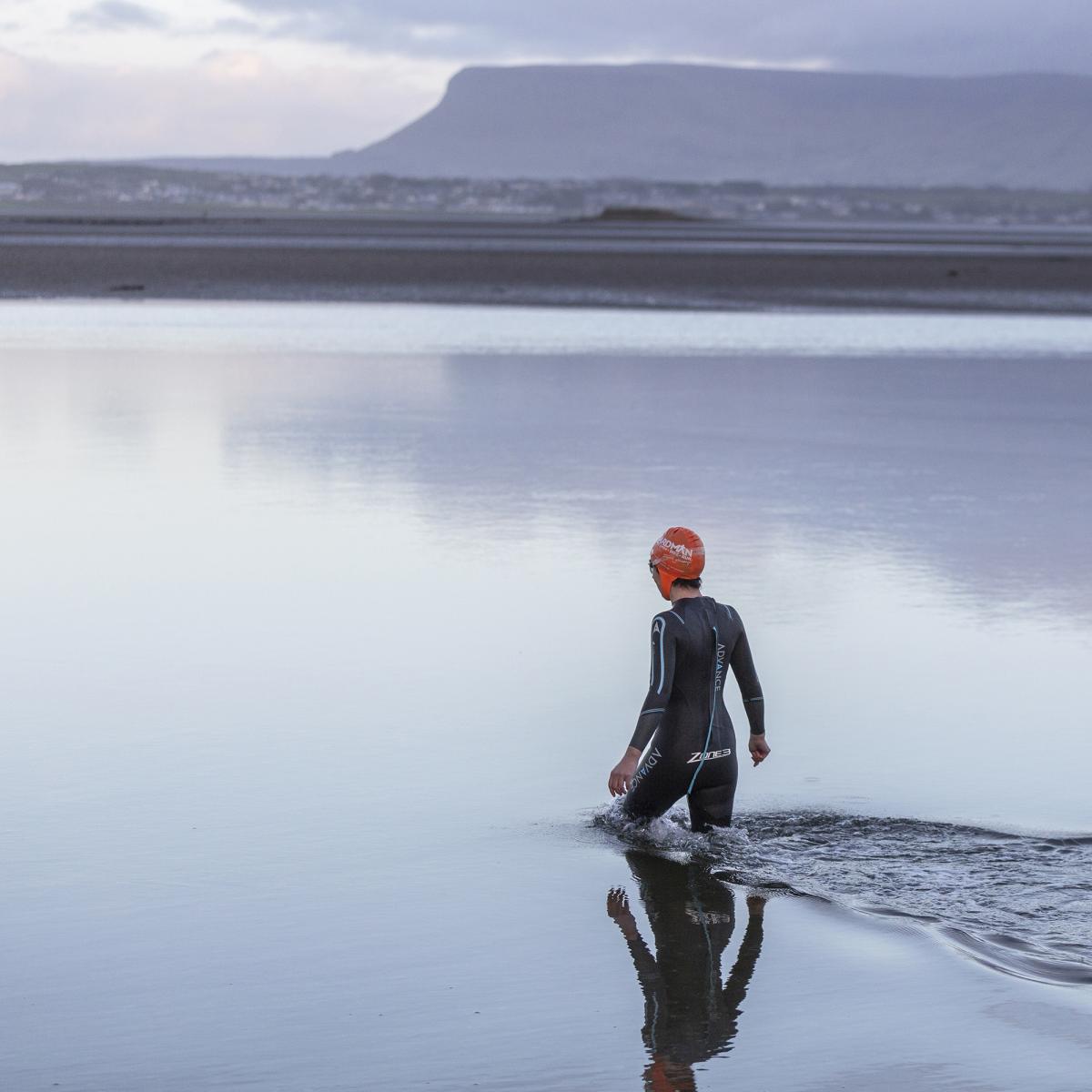 Swimmer walks in to the sea with the mountains in the background
