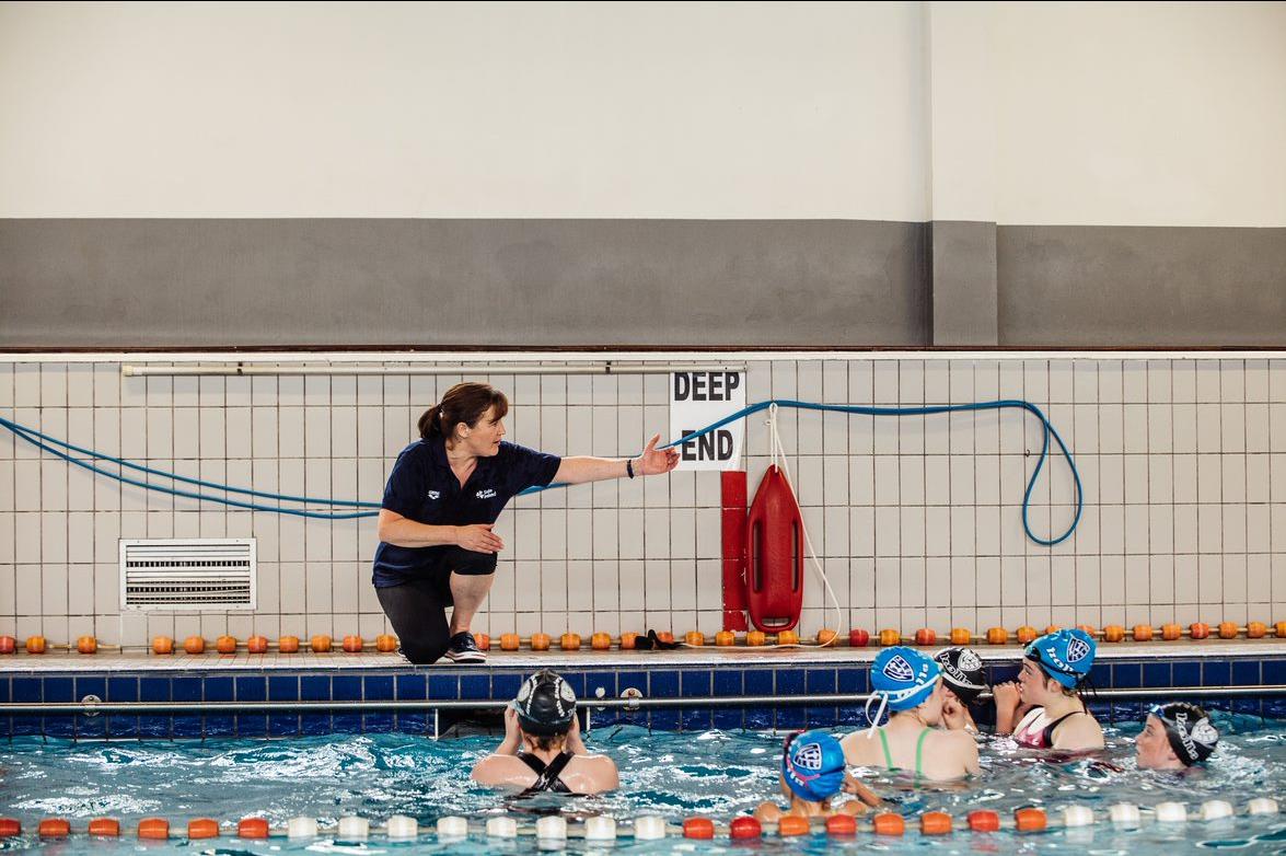 A swim coach instructs a group of female swimmers in a pool