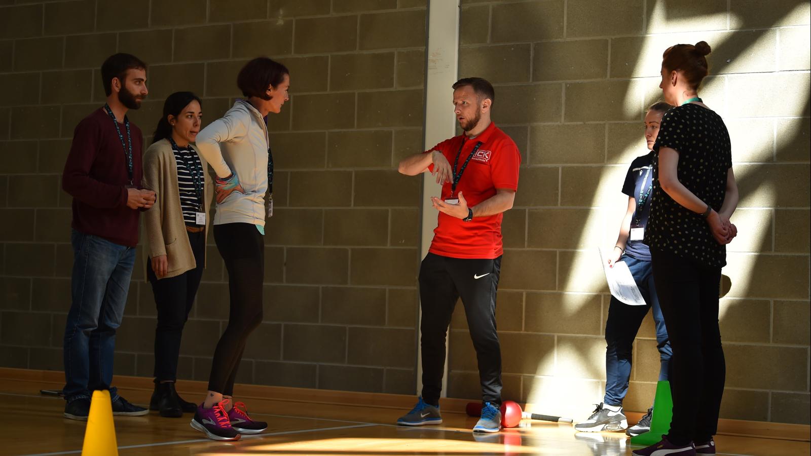 A coach addresses a group of students in a sports hall